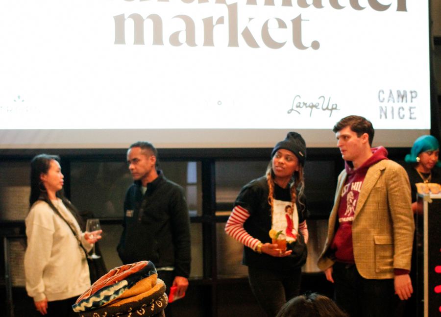 Guests talking over drinks in front of the Mindful Matter Market banner at an evening gathering