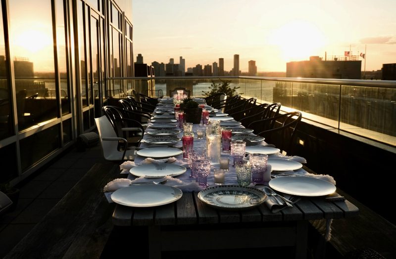 A long table laid for a Mindful Matter Market farm-to-table dinner on a Manhattan rooftop at sunset, overlooking the Hudson