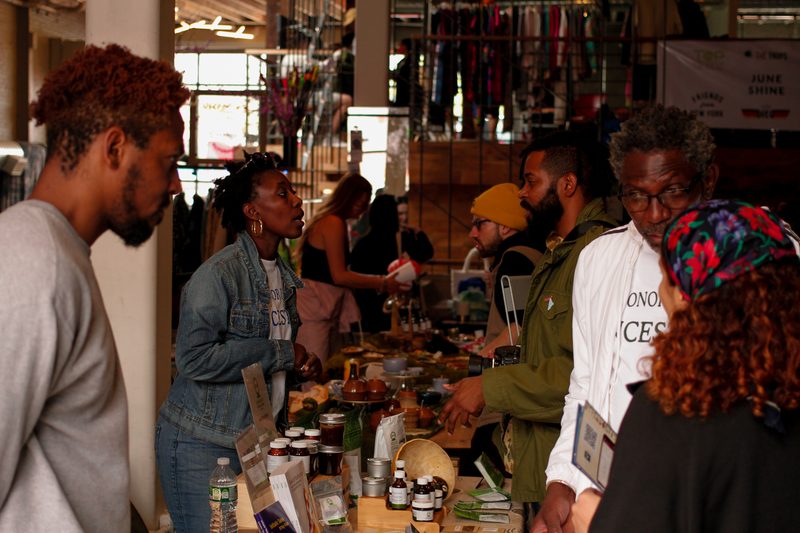 Visitors browsing a vendor table of tinctures, oils and botanical wellness goods at a Mindful Matter Market seasonal market